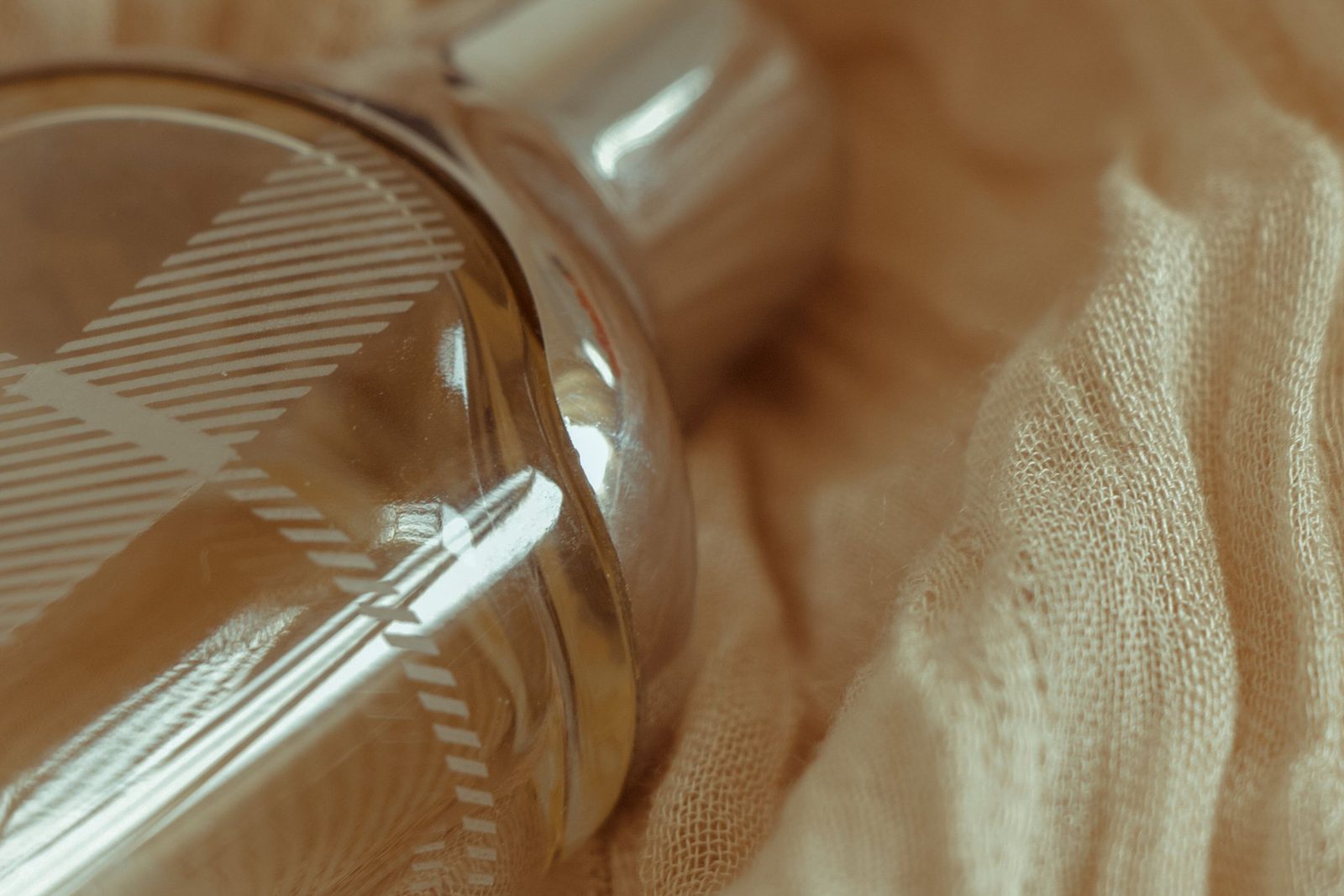 Szklany flakon perfum leżący na beżowej tkaninie
